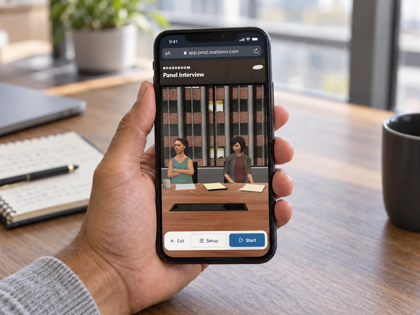 A hand holding a smartphone with Ovation Panel Interview practice open in a browser in an office
